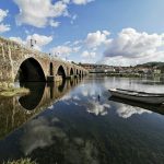 white wooden row boat on clear water near bridge under blue sky and white clouds during day time