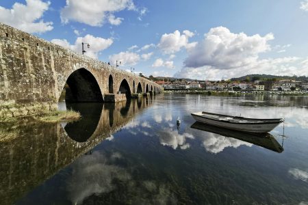 white wooden row boat on clear water near bridge under blue sky and white clouds during day time