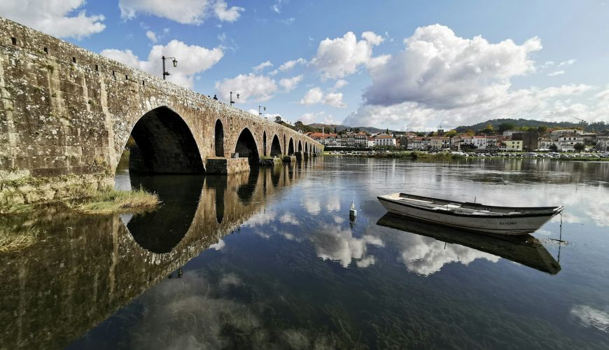 white wooden row boat on clear water near bridge under blue sky and white clouds during day time